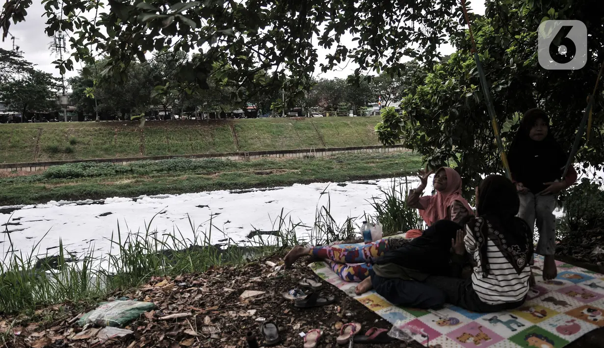 Warga bersantai di dekat limbah busa yang memenuhi aliran Kanal Banjir Timur (KBT), Duren Sawit, Jakarta, Kamis (2/7/2020). Busa yang memenuhi aliran KBT akibat limbah pabrik dan rumah tangga sejak dua minggu lalu itu menjadi tontonan warga meski menimbulkan bau tak sedap (merdeka.com/Iqbal Nugroho)