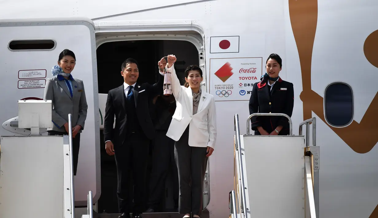 Dua atlet peraih tiga kali medali emas olimpiade Tadahiro Nomura (kedua kiri) dan Saori Yoshida (kedua kanan) membawa api untuk obor Olimpiade Tokyo 2020 saat tiba dari Yunani di Pangkalan Udara Matsushima, Prefektur Miyagi, Jepang, Jumat (20/3/2020). (Philip FONG/AFP)