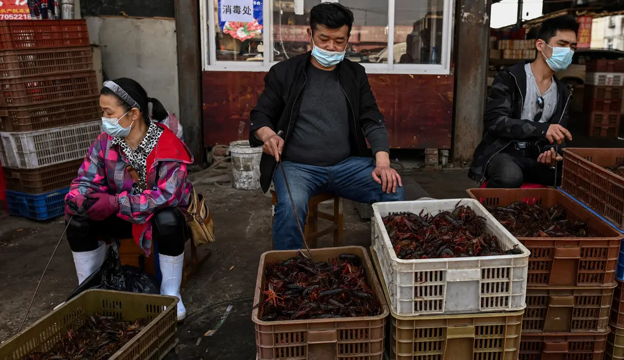 Pedagang mengenakan masker saat menawarkan udang untuk dijual di Pasar Baishazhou Wuhan di Wuhan, provinsi Hubei, Rabu (15/4/2020). Lebih dari 90 persen kios pasar basah di Wuhan telah kembali buka sejak pemerintah mencabut aturan lockdown di wilayah pusat wabah tersebut. (Hector RETAMAL/AFP)