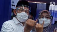 Calon Wali Kota Depok nomor urut 2 Mohammad Idris didampingi istrinya Elly Farida menunjukkan jari yang telai ditandai dengan tinta usai menggunakan hak pilinya dalam  Pilkada Depok 2020 di TPS 14 Jatimulya, Depok, Rabu (9/12/2020).. (Liputan6.com/Herman Zakharia)