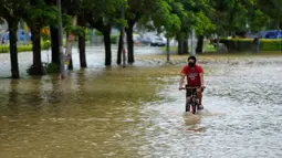Seorang pria bersepeda menerjang banjir di Batu Berendam, Malaka, Malaysia, 3 Januari 2022. Tercatat ada tujuh negara bagian Malaysia yang diterjang banjir pada 2 Januari 2022. (NAZRULHAD HASHIM/AFP)