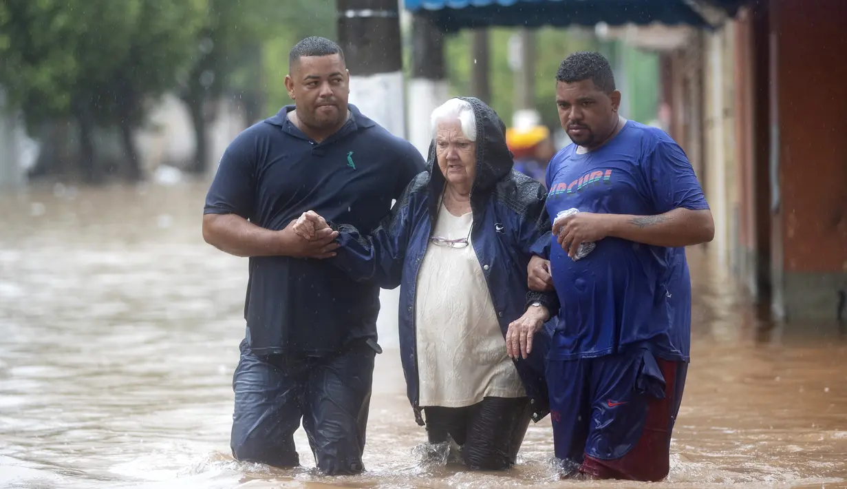 Dua pria membantu seorang wanita menyeberangi jalan yang banjir di Sao Paulo, Brasil, Senin, (10/2/2020). Hujan deras yang membanjiri kota, menyebabkan pinggir sungai utama meluap. (AP Photo/Andre Penner)