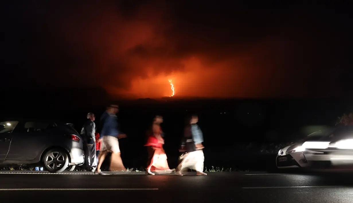 Warga berjalan kaki saat lava pijar keluar dari gunung api Piton de la Fournaise atau Peak of the Furnace di Pulau Reunion, Samudera Hindia, Prancis, Selasa (13/8/2019). Letusan Piton de la Fournaise berlanjut hingga hari ketiga. (Richard BOUHET/AFP)