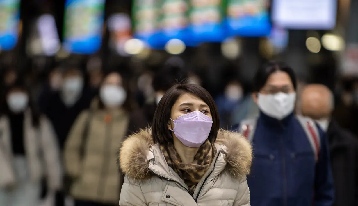 Seorang wanita memakai masker berjalan di stasiun Shinagawa di Tokyo (18/1/2022). Jepang melaporkan rekor tertinggi infeksi Covid-19 baru yang dipicu oleh varian Omicron. (AFP/Philip Fong)
