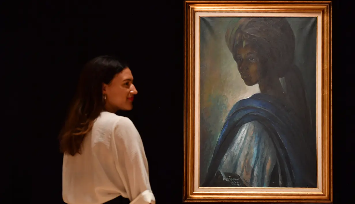 Karyawan rumah lelang Bonhams berpose dekat lukisan seorang putri Nigeria bernama Tutu di London, Inggris pada 7 Februari 2018. Lukisan yang kerap disebut ‘Mona Lisa dari Afrika’ itu terjual dalam sebuah lelang pada 28 Februari 2018. (BEN STANSALL/AFP)