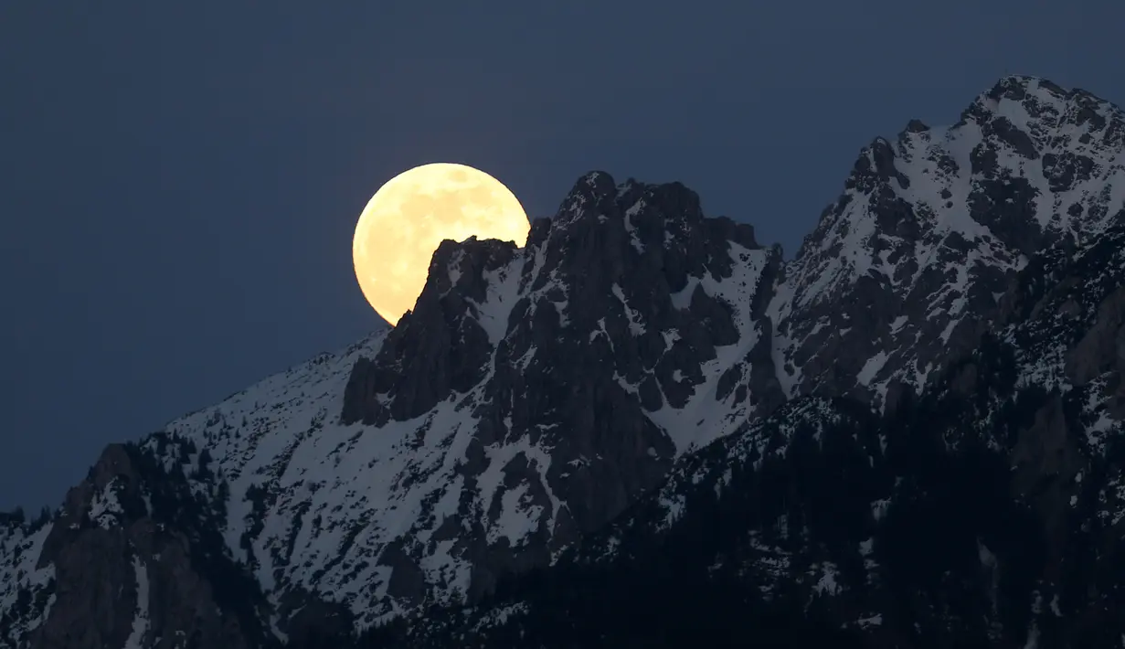 Bulan purnama tampak di belakang pegunungan Alpen yang tertutup salju di Buching, Jerman selatan, (10/5). (Karl-Josef Hildenbrand/dpa/AFP)