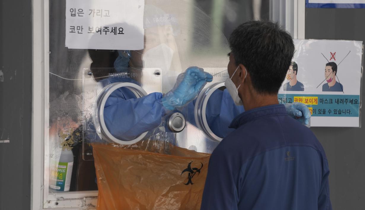Pekerja medis mengenakan alat pelindung di bilik, mengambil sampel pengunjung di klinik skrining sementara untuk virus corona di Seoul, Korea Selatan, Jumat (24/9/2021). Lonjakan harian virus corona terjadi usai orang-orang kembali liburan terbesar di negara itu tahun ini. (AP Photo/Lee Jin-man)