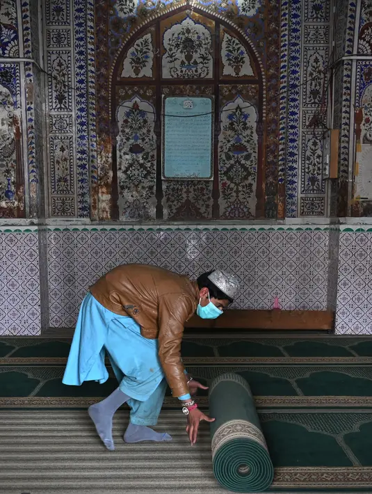 Umat Muslim menggulung karpet sajadah dari aula utama masjid menyusul pembatasan baru pemerintah baru menjelang bulan suci Ramadan di Rawalpindi, Pakistan, Senin (5/4/2021). Salat akan dilakukan di  halaman di masjid dan bukan di dalam aula. (Aamir QURESHI/AFP)