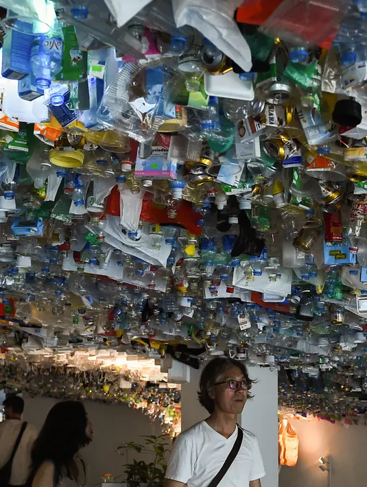 Pengunjung melihat instalasi seni yang terbuat dari sisa-sisa plastik, kaleng dan wadah di sebuah pameran "Reduce the Litter" di Hanoi (15/7/2019). Pameran ini menggambarkan polusi dari limbah rumah tangga yang menyebabkan dampak berbahaya bagi lingkungan dan kesehatan anak. (AFP Photo/Nhac Nguyen)