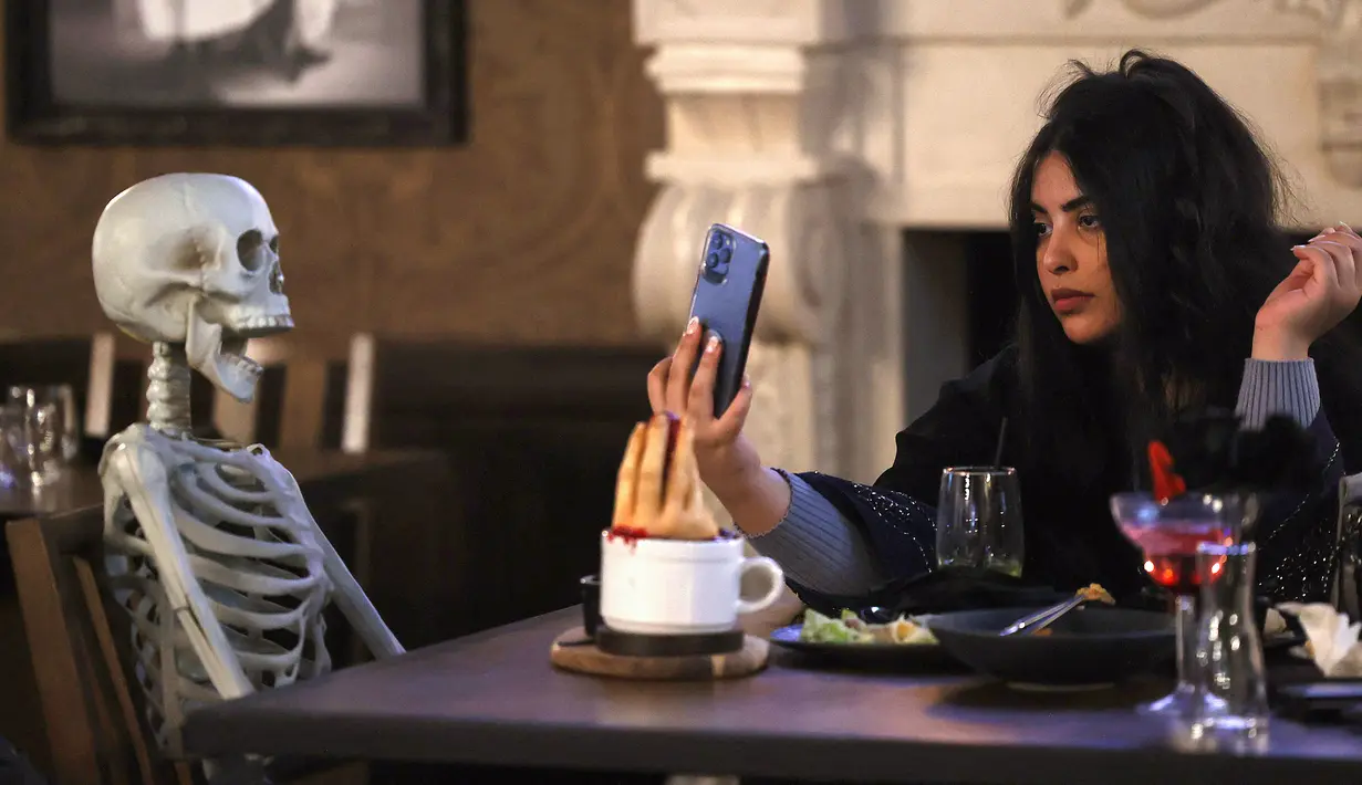Pengunjung mengambil gambar tengkorak yang duduk di mejanya di restoran "Shadows" bertema horor di Riyadh, Arab Saudi, 19 Januari 2022. Restoran tersebut menawarkan pengalaman unik kepada pelanggan dari hidangan dengan tengkorak dan darah ditemani zombie serta vampir (Fayez Nureldine/AFP)