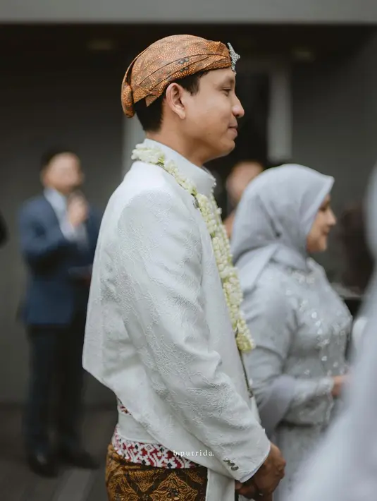 Sang suami mengenakan beskap putih, lengkap dengan kain batik serasi yang juga dikenakan Nessie Judge, dan blangkonnya. [Foto: Instagram/thebridestory]