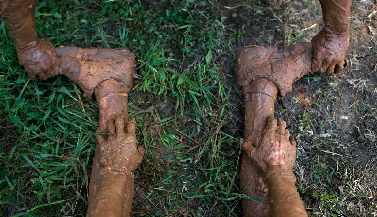 Seorang peserta membantu meregangkan kaki rekannya saat mengikuti Mud Day di Tel Aviv, Israel (24/3). Sekitar 5.000 orang ikut berpartisipasi dalam lomba Hari Lumpur di Tel Aviv ini. (AP Photo/Oded Balilty)