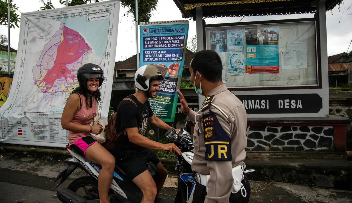 Turis asal Prancis, Anna Mangler (kiri) dan rekannya dari Jerman diberhentikan oleh polisi saat ingin memasuki area terlarang untuk melihat aliran lahar dingin Gunung Agung di Karangasem, Bali (29/11). (AFP Photo/Juni Kriswanto)