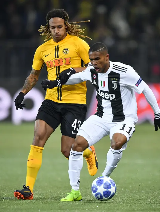 Bek Young Boys, Kevin Mbabu berebut bola  dengan pemain Juventus, Douglas Costa pada laga pamungkas Grup H Liga Champions di Stade de Suisse, Kamis (13/12). Kalah 1-2, Juventus tetap keluar sebagai juara Grup H. (Fabrice COFFRINI/AFP)