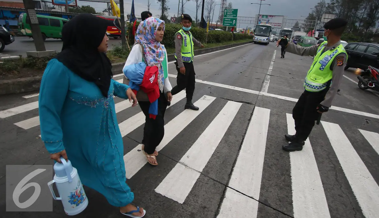 Petugas kepolisian membantu warga menyeberang jalan di Perempatan Cileunyi, Jawa Barat, Jumat (1/7). Mulai banyaknya kendaraan pemudik membuat petugas kepolisian membantu pejalan kaki yang ingin menyeberang. (Liputan6.com/Immanuel Antonius) 