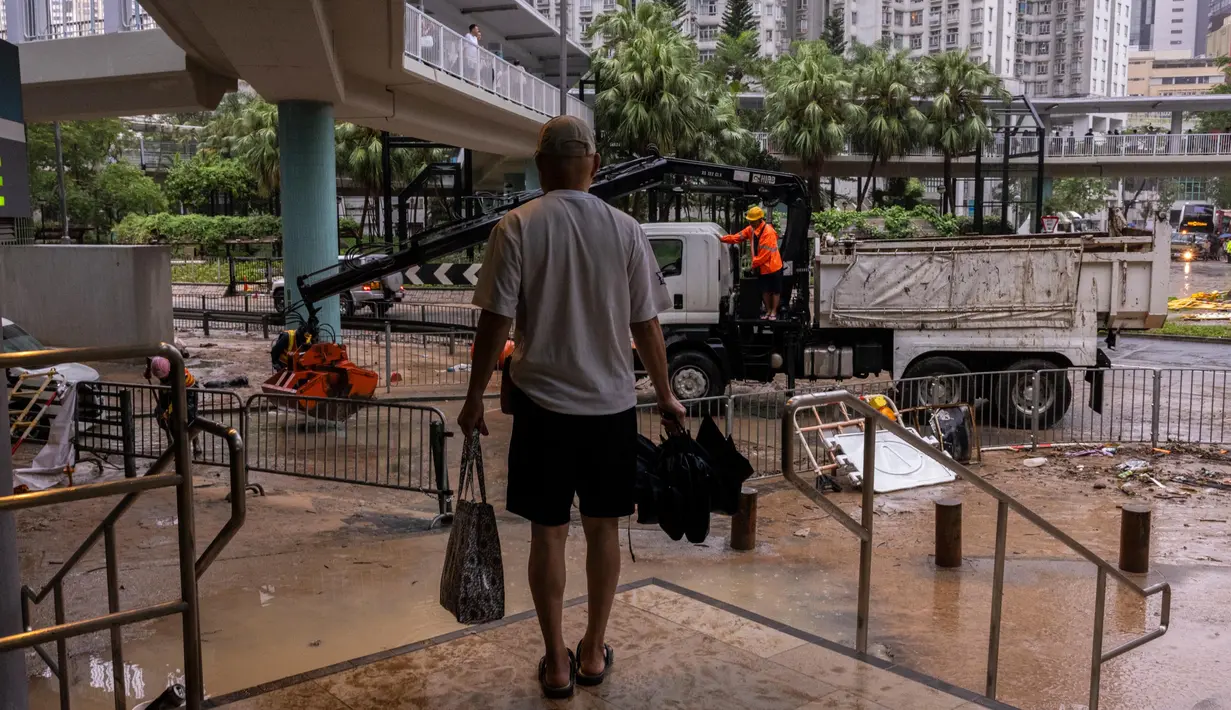 Hujan lebat dengan curah tertinggi selama 140 tahun terakhir terus turun sejak Kamis (7/9). Tampak, pejalan kaki berdiri di tempat yang lebih tinggi di dekat jalan yang tergenang air setelah hujan deras di Hong Kong, Jumat, 8 September 2023. (AP Photo/Louise Delmotte)