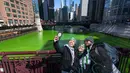 Sekelompok orang berselfie dengan latar belakang Sungai Chicago yang berwarna hijau di LaSalle Street Bridge, Sabtu (12/3/2022). Perubahan warna ini dilakukan untuk menyambut Hari St. Patrick pada Kamis mendatang. (Tyler Pasciak LaRiviere/Chicago Sun-Times via AP)