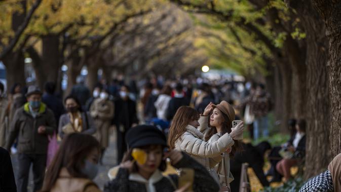 Orang-orang mengambil foto saat mereka berjalan melalui barisan pohon ginkgo saat pepohonan dan trotoar ditutupi dedaunan kuning cerah di sepanjang trotoar di Tokyo, Jepang pada 28 November 2020. (AP Photo/Kiichiro Sato)