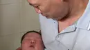 Tran Van Quan menggendong bayi laki-lakinya, Tran Tien Quoc di pusat kesehatan Vinh Tuong, provinsi Vinh Phuc, Vietnam, Minggu (15/10). Bayi laki-laki tersebut lahir melalui operasi Caesar pada 14 Oktober 2017 lalu. (LE PHUONG/AFP)