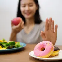 Seorang perempuan menolak sepiring donat dan hendak memakan buah serta sayuran (Foto Dok: Freepik/skawee).