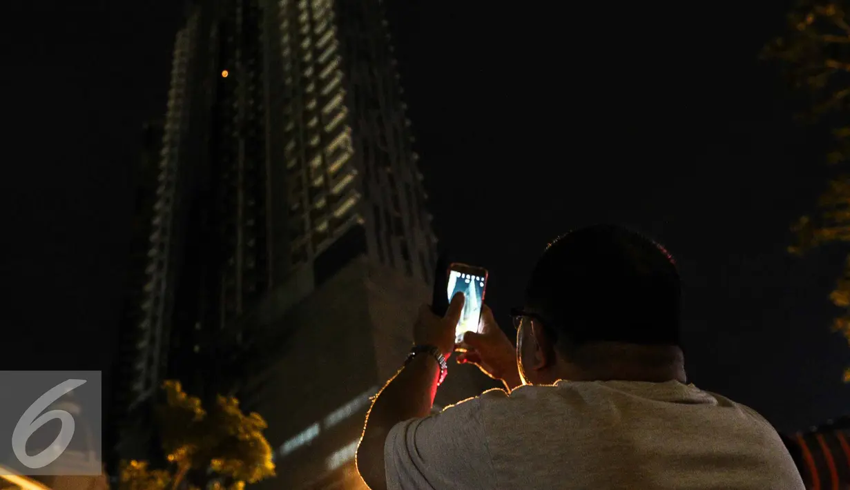 Warga mengabadikan titik api yang masih tersisa di Gedung Neo Soho, Jakarta Barat, Rabu (9/11). Gedung Neo Soho sempat terbakar hebat hampir di setiap lantainya. (Liputan6.com/Faizal Fanani)