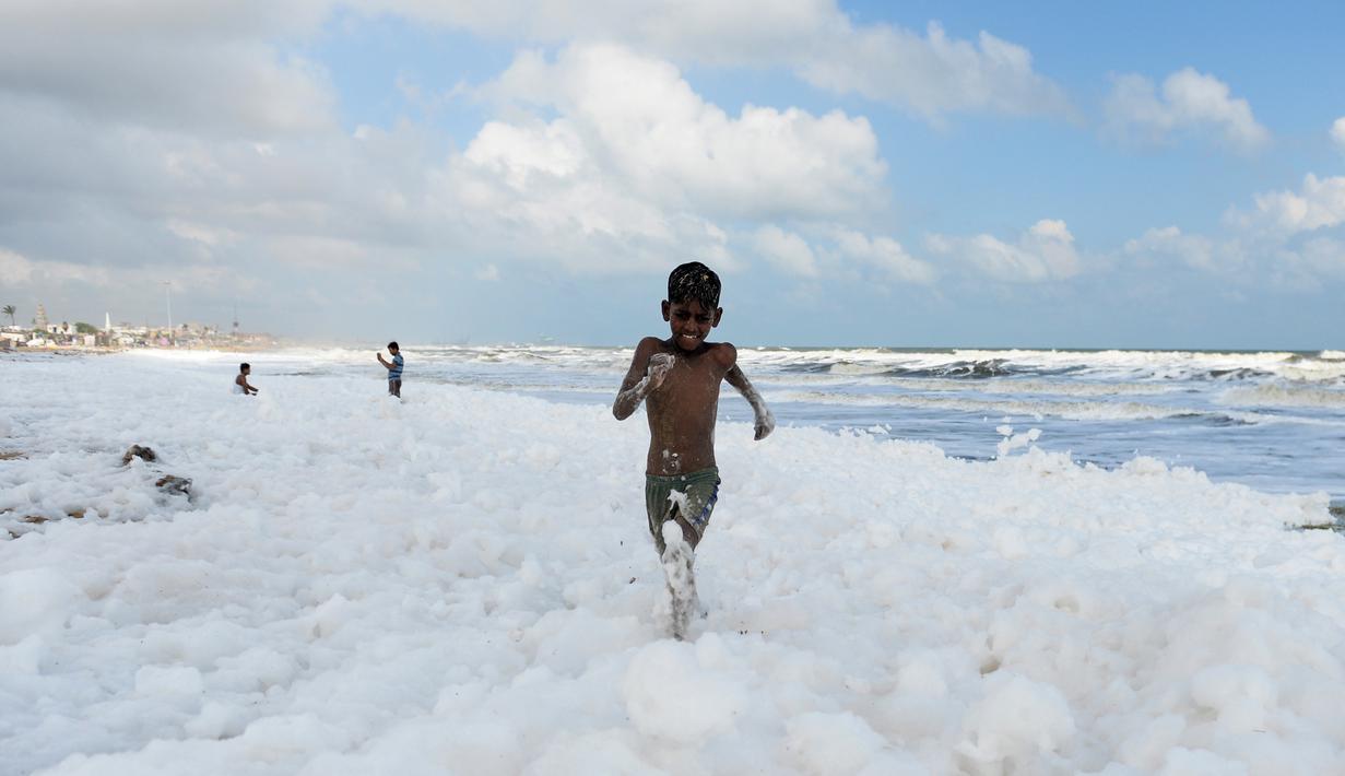 Seorang anak berlari di atas limbah busa yang disebabkan polutan saat bercampur dengan ombak di pantai di Chennai (29/11/2019). Limbah mencapai laut melalui sungai, memicu busa beracun di pantai tersebut. (AFP/Arun Sankar)