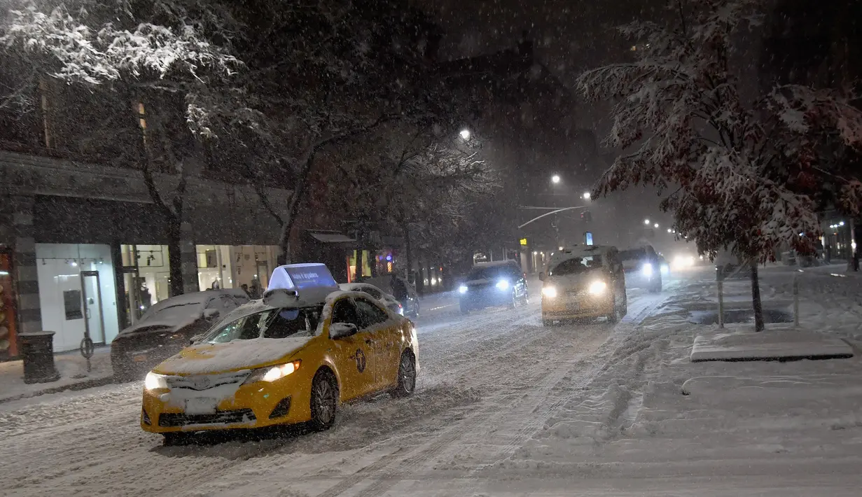 Mobil-mobil melaju saat salju mulai turun di Manhattan, New York, Kamis (15/11). Layanan Cuaca Nasional memprediksi hujan salju pertama pada awal musim dingin itu akan mencapai ketebalan 2-4 inci. (Angela Weiss / AFP)
