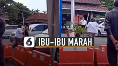 Seorang ibu-ibu mengenakan seragam putih membawa tongkat sambil marah-marah kepada seorang SPG.