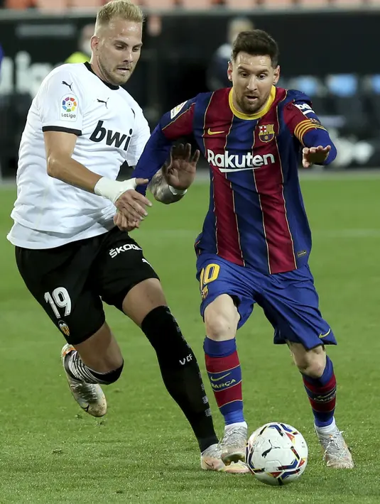 Penyerang Barcelona, Lionel Messi membawa bola dari kawalan pemain Valencia, Uros Racic pada pertandingan La Liga Spanyol di stadion Mestalla, Senin (3/5/2021). Barcelona menang tipis atas Valencia 3-2. (AP Photo/Alberto Saiz)