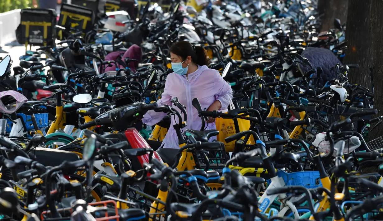 Seorang wanita berjalan melintasi sepeda-sepeda yang diparkir di atas trotoar di Beijing, China (21/7/2020). Seperti diketahui Beijing telah menerapkan bike sharing yang sudah tersedia di trotoar-trotoar Kota Beijing. (AFP Photo/Greg Baker)