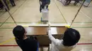 Perwakilan dari komisi administrasi pemilihan lokal menyaksikan para pemilih memberikan suara mereka untuk pemilihan majelis rendah di sebuah TPS, Tokyo, Jepang, Minggu (31/10/2021). Jepang menggelar Pemilu di tengah pandemi COVID-19. (AP Photo/Eugene Hoshiko)