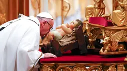 Paus Fransiskus mencium patung bayi Yesus saat memimpin misa Natal di Basilika Santo Petrus, Vatikan, (24/12).  Pada misa tersebut, Paus mengatakan bahwa Natal sudah "disandera" oleh materialisme. (REUTERS/Tony Gentile)