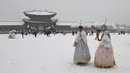 Pengunjung yang mengenakan pakaian tradisional hanbok berjalan di tengah salju di istana Gyeongbokgung di pusat kota Seoul, Korea Selatan, Sabtu (30/12/2023). (Jung Yeon-je / AFP)