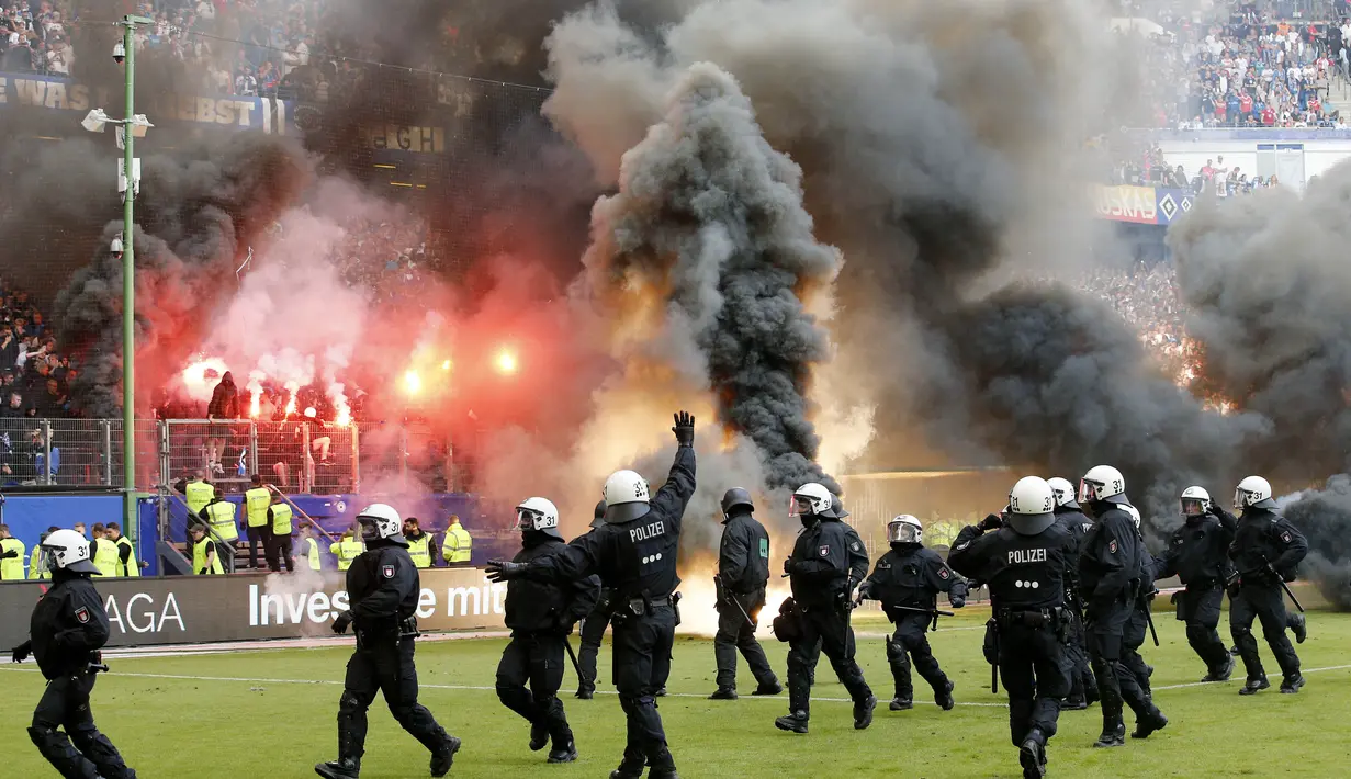 Petugas kepolisian berusaha menenangkan suporter yang mengamuk saat pertandingan antara Hamburg SV melawan VfL Borussia Moenchengladbach di Volksparkstadion, Sabtu (12/5/2018). Hamburg SV terdegradasi dari Bundesliga Jerman. (AP/Michael Sohn)