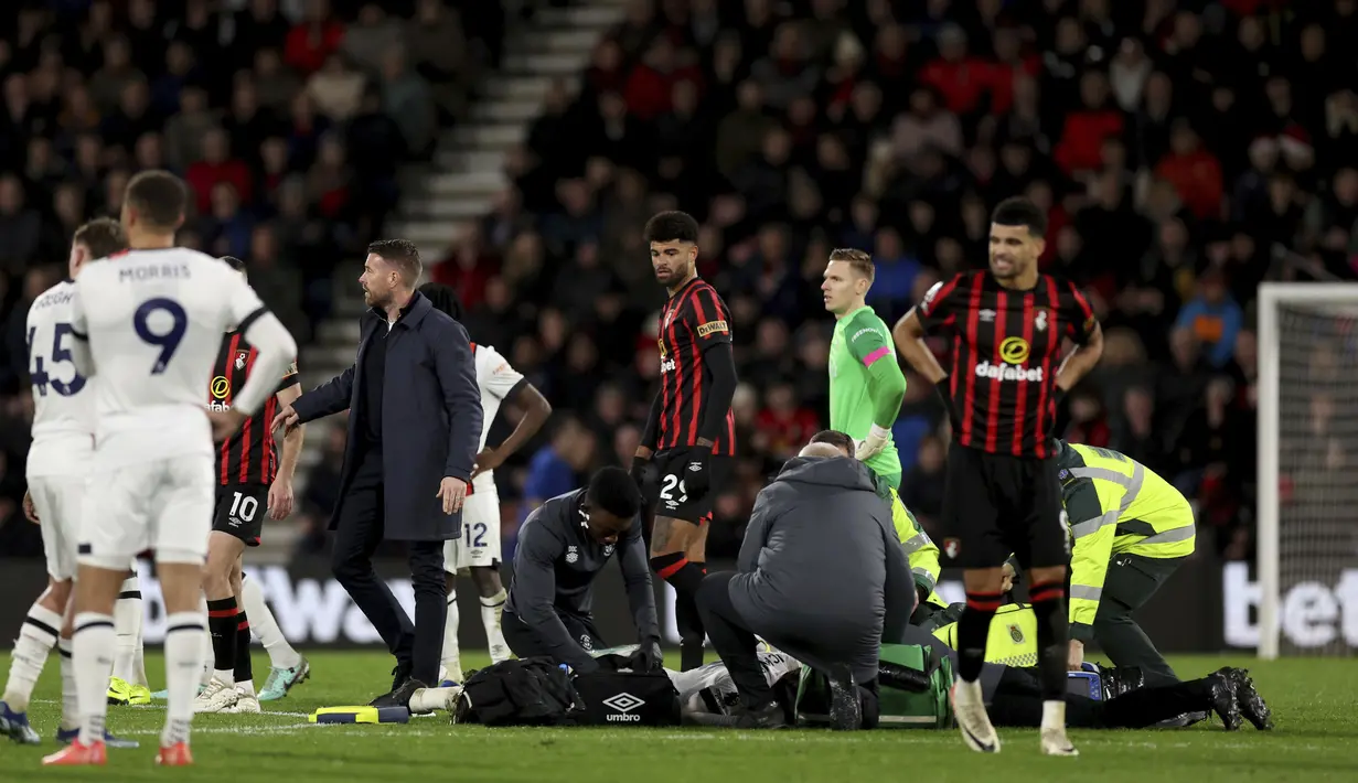 <p>Petugas medis menolong pemain Luton Town, Tom Lockyear yang mengalami pingsan secara tiba-tiba di tengah lapangan dalam pertandingan Liga Inggris 2023/2024 antara Bournemouth melawan Luton Town yang berlangsung di Vitality Stadium, Sabtu (16/12/2023). (AP/PA/Steven Paston)</p>