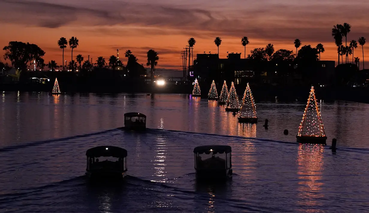 Perahu melewati lampu pohon Natal yang mengapung di Long Beach, California, Minggu (19/12/2021). Sambut Natal, pantai di California menghiasi pantainya dengan hiasan lampu pohon Natal. (AP Photo/Ashley Landis)