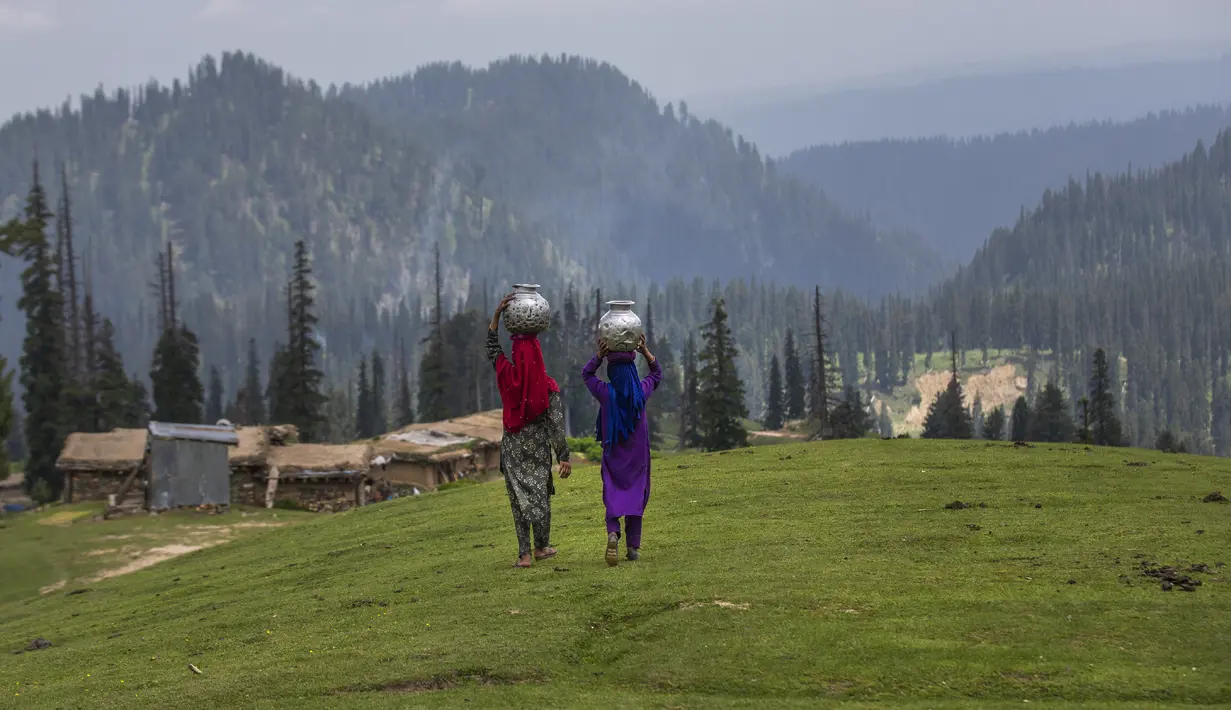 Gadis-gadis penggembala Kashmir berjalan pulang setelah mengambil air dari mata air terdekat di Tosamaidan, barat daya Srinagar, Kashmir yang dikuasai India, Senin (21/6/2021).  Padang rumput Tosamaidan ini dulunya merupakan tempat tembak artileri tentara India. (AP Photo/Dar Yasin)