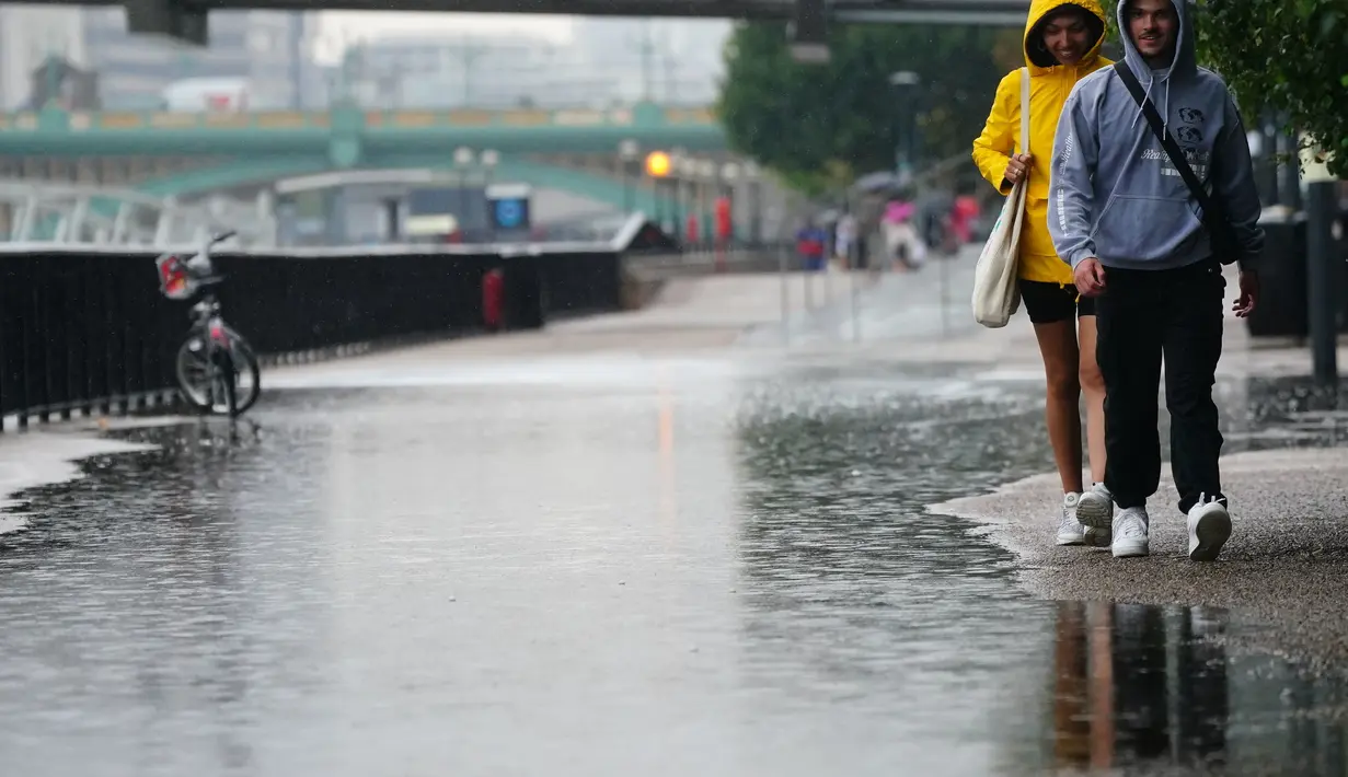 Orang-orang berjalan di tengah hujan di London, Rabu (17/8/2022). Setelah berminggu-minggu cuaca terik, yang telah menyebabkan kekeringan dan membuat tanah kering, peringatan badai petir kuning dari Kantor Meteorologi memperkirakan hujan lebat dan badai petir yang bisa melanda bagian Inggris dan Wales. (Victoria Jones/PA via AP)