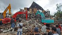 Sejumlah warga menyaksikan alat berat mencari korban di reruntuhan gedung pemerintah daerah yang runtuh saat gempa bumi di Mamuju, Sulawesi Barat, Jumat (15/1/2021). (AP Photo/Azhari Surahman)