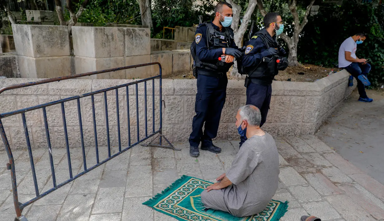Dua anggota pasukan keamanan Israel berjaga saat seorang jemaah Palestina melaksanakan salat Jumat selama bulan suci Ramadan di tengah krisis pandemi coronavirus di luar kompleks masjid al-Aqsa di Kota Tua Yerusalem (15/5/2020). (AFP/Ahmad Gharabli)