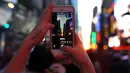 Seorang wanita mengambil gambar fenomena Manhattanhenge, dimana matahari terbenam sejajar tepat dengan jalan, di Times Square, New York City, Kamis (12/7). Manhattanhenge dimana saat matahari terbenam sejajar dengan jalan. (AFP/TIMOTHY A. CLARY)