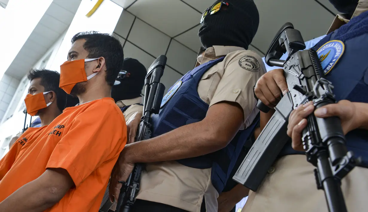 Petugas Badan Narkotika Nasional Indonesia (BNN) mengawal dua pria lokal yang diduga menyelundupkan sabu pada konferensi pers di Banda Aceh (13/10/2020). (AFP Photo/Chaideer Mahyuddin)