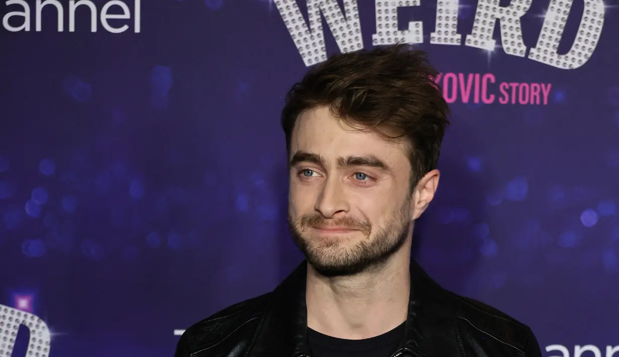 Daniel Radcliffe berpose sambil tersenyum saat menghadiri pemutaran perdana film "Weird: The Al Yankovic Story" di Alamo Drafthouse Cinema Downtown Brooklyn di New York pada Selasa, 1 November 2022. Aktor berbakat itu tampil dengan rambut cokelatnya yang sedikit acak-acakan dan memakai sedikit tengkuk. (Theo Wargo/Getty Images/AFP)