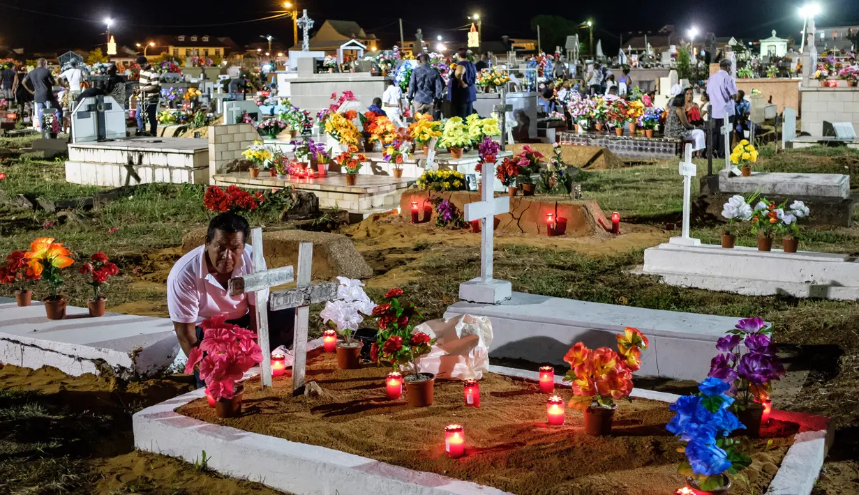 Seorang pria menaruh bunga di makam keluarganya yang berada di pemakaman Cayenne di Guyana Prancis (1/11). Mereka mengunjungi makam keluarganya dalam perayaan All Saints Day. (AFP Photo/Jody Amiet)