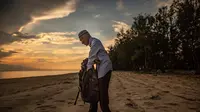 Tengku Mohamad Ali Mansor memeriksa botol kaca di sebuah pantai di desa Mangkuk, Malaysia timur pada 12 September 2020.  Upaya seorang lansia Malaysia untuk membersihkan pantai-pantai negara itu dari kaca-kaca yang terkelupas membuatnya mengumpulkan koleksi ribuan botol. (AFP/Mohd Rasfan)