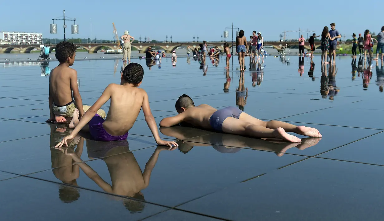 Sejumlah anak tidur di lantai saat menikmati bermain air mancur pada musim panas di pusat kota Bordeaux, Prancis barat daya, Senin (19/6). Saat ini suhu temperatur di Prancis mencapai 36 derajat celcius. (AFP Photo / NICOLAS TUCAT)