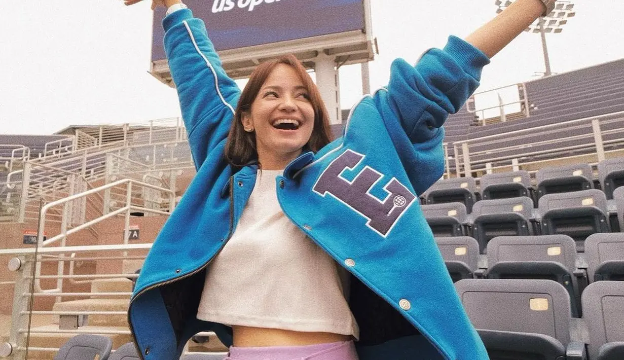 Nonton final US Open bersama rombongan Erigo, Enzy Storia tampil sporty kasual memadukan crop top putih sebagai inner dan jaket biru sebagai outer. Kesan feminin pun ditambahkan lewat celana rok  berwarna lilac yang ia kenakan sebagai bawahan.  (Instagram/enzystoria).