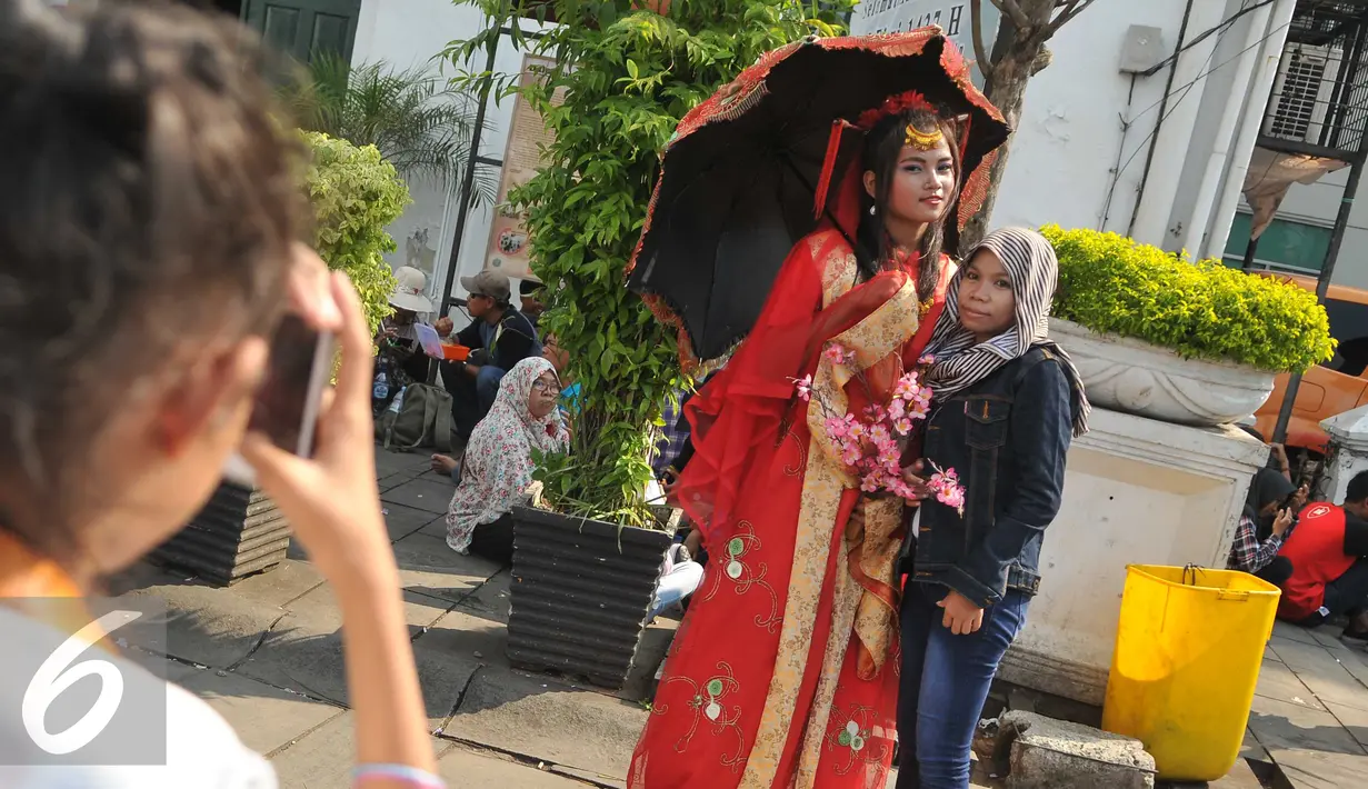 Seorang pengunjung berpose dengan wanita berkostum ala Tionghoa saat mengunjungi Kota Tua, Jakarta, Jumat (8/7). Kota Tua menjadi salah satu pilihan masyarakat Jakarta ataupun luar Jakarta, untuk mengisi libur lebaran. (Liputan6.com/Gempur M Surya)