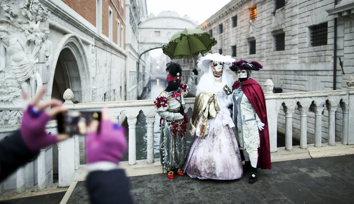 Wisatawan mengambil gambar sejumlah peserta yang menggunakan kostum dan topeng di depan Ponte dei Sospiri (Bridge of Sighs) saat mengikuti Karnaval Venesia, Italia, Sabtu (30/1). (REUTERS/Alessandro Bianchi)