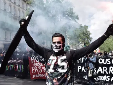 Seorang pria memegang bendera sambil manyalakan suar asap saat demonstrasi perayaan May Day di Paris, Prancis,Senin (1/5). Hari Buruh Internasional atau May Day di Paris, diwarnai bentrokan antara pengunjuk rasa dengan polisi.  (PHILIPPE LOPEZ/AFP)